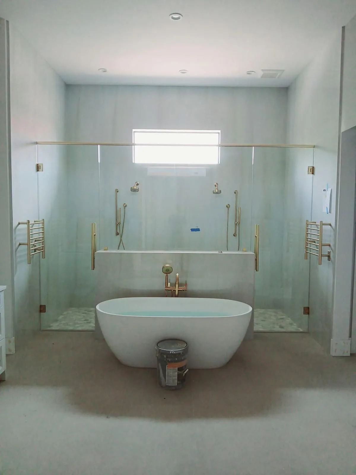 Spacious bathroom with a freestanding bathtub between two glass shower enclosures; gold fixtures.