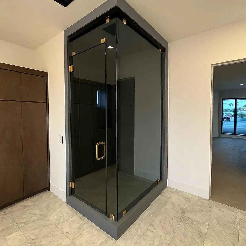 Corner shower with dark gray frame and tinted glass. Gold-toned hardware, set in a marble-tiled bathroom.