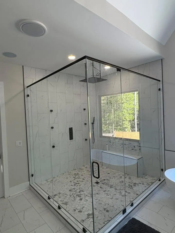 A modern, glass-enclosed shower with black hardware, white tile, and a bench inside.